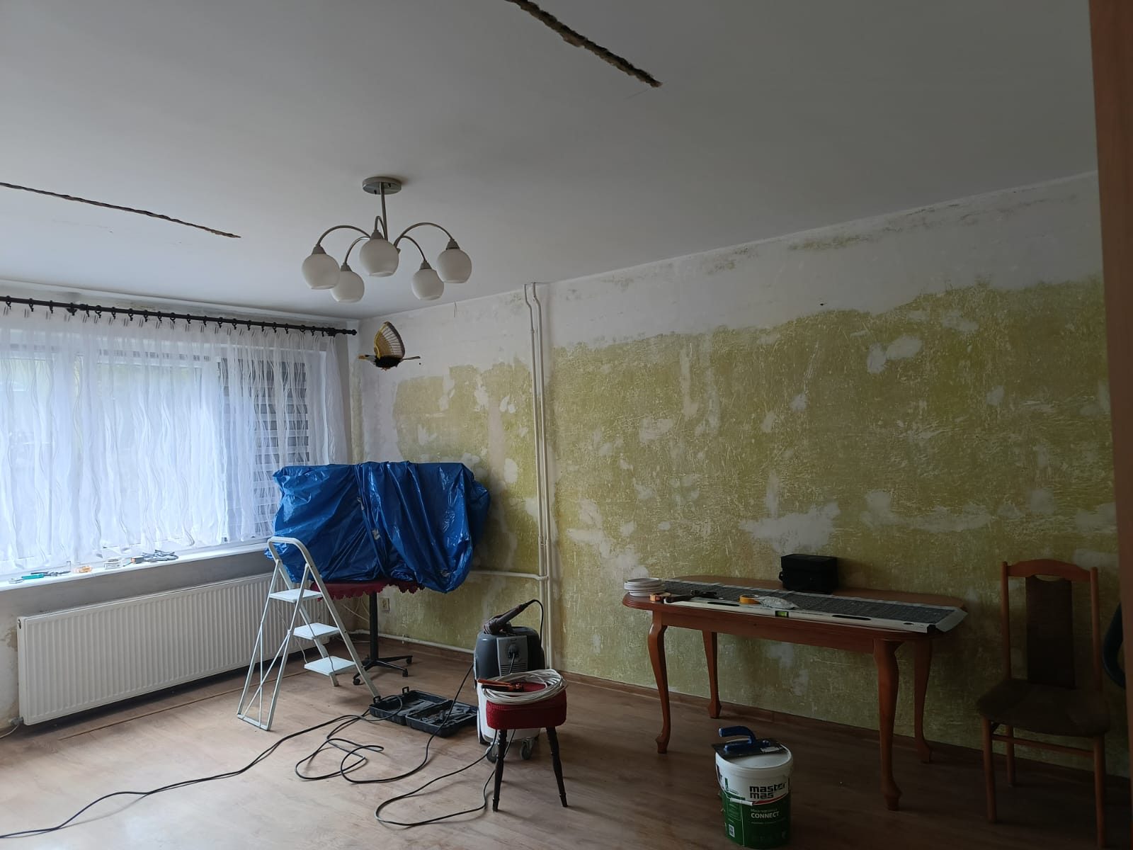Pokój dzienny przed remontem — zerwane tapety, zabezpieczone meble i narzędzia — LUX-BUD